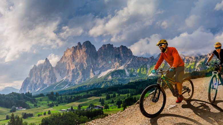 A cyclist on a mountain road, between cliffs and pine forests.